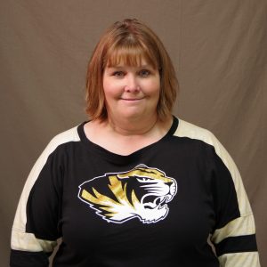white woman with mid-length auburn hair wearing a black and white Mizzou shirt with a tiger head