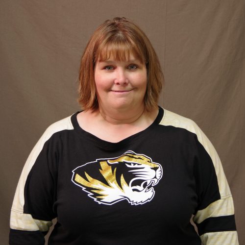 white woman with mid-length auburn hair wearing a black and white Mizzou shirt with a tiger head
