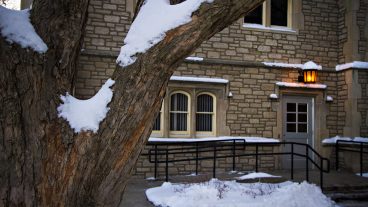Snow covers a tree limb with a stone building in the background