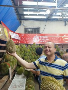 A man is holding a durian fruit in a market.