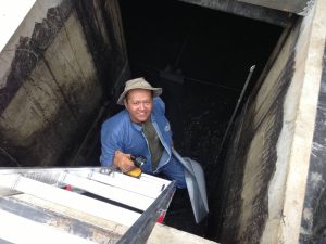 A man is descending into hole in the ground via a ladder. he looks up and smiles at the camera.
