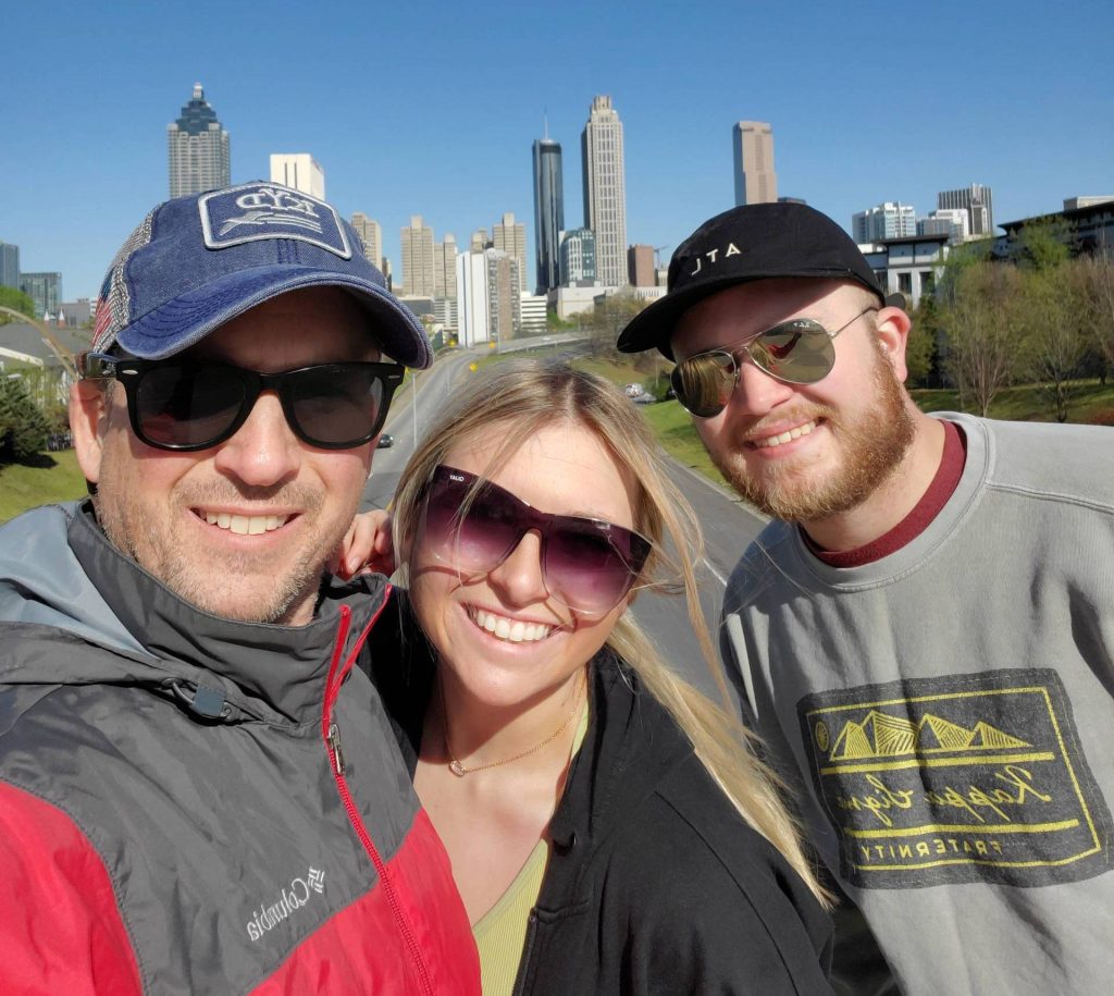 2 men and one woman pose in front of a city skyline