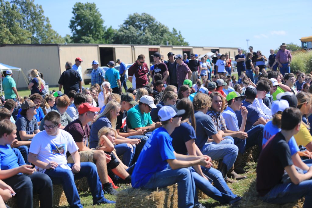 a large group of students wearing colorful shirts gather on hay bales at an outdoor event