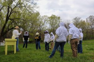 A group of people stand outside in a grassy field in beekeeper gear.