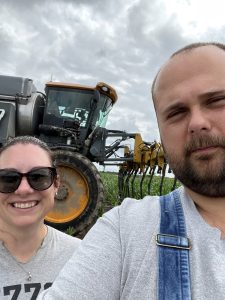 Nick and a woman stand in front of a tractor to smile for a selfie.
