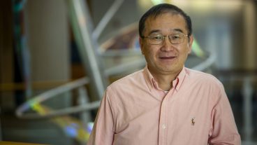 An Asian man in glasses and a long-sleeved, pale pink button-up shirt