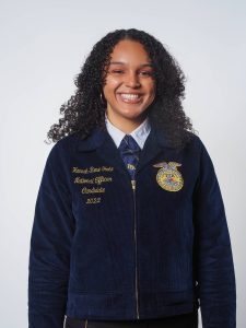 A young, black woman wearing a Future Farmers of America jacket that reads "Hannah-Rose Foote National Officer Candidate 2022". She is smiling in front of a grey background.
