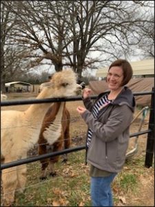 A woman is smiling at the camera while she feeds a llama.