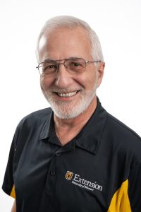 Headshot of Hank Stelzer. Man with white hair and glasses wearing a black and gold polo shirt