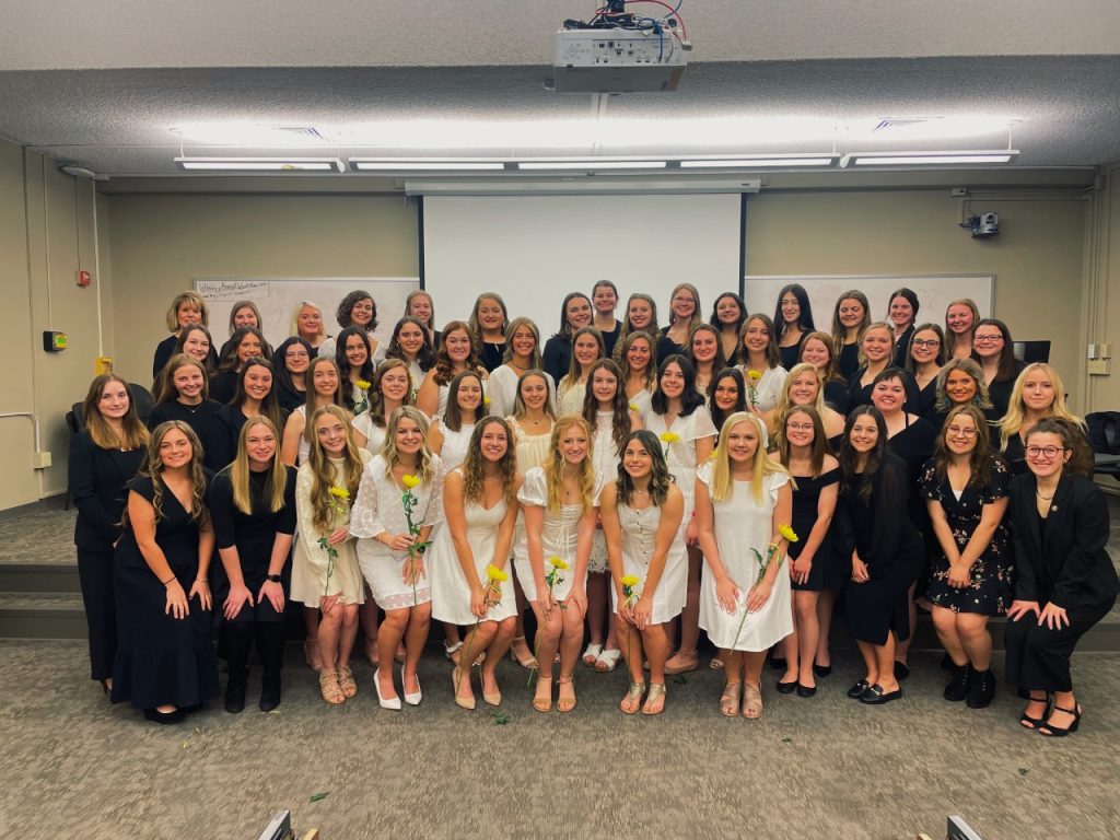 Photo of the Sigma Alpha chapter. A large group of women pose for a photo, some wearing black dresses and some wearing white