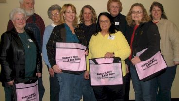 A group of nine people pose together for a photo holding pink bags.