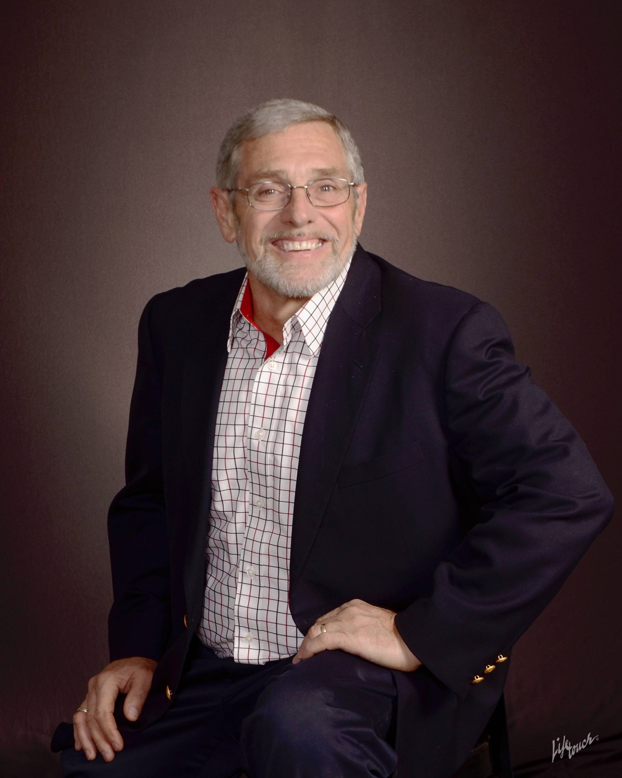 older white man with gray hair, wearing a white checkered shirt with a dark sportcoat, posing in a studio