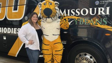 A woman and Truman the Tiger standing in front of the Mizzou football bus.