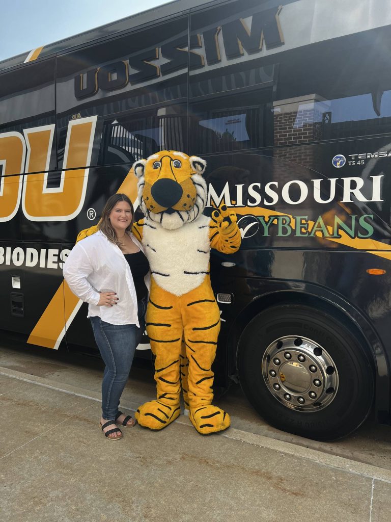 A woman and Truman the Tiger standing in front of the Mizzou football bus.