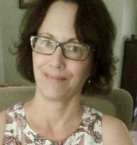 white woman with glasses and short brown hair, wearing a sleeveless floral shirt