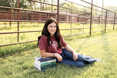 Chloe Collins laying in field of grass in front of a fence. 