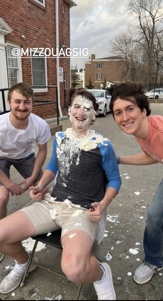 A student. who has been pied in the face, poses for a photo with two other students. 