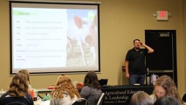 A student presents a PowerPoint presentation to a room of other students.