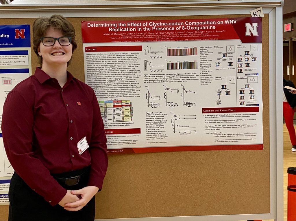 A student poses for a photo next to a research poster.