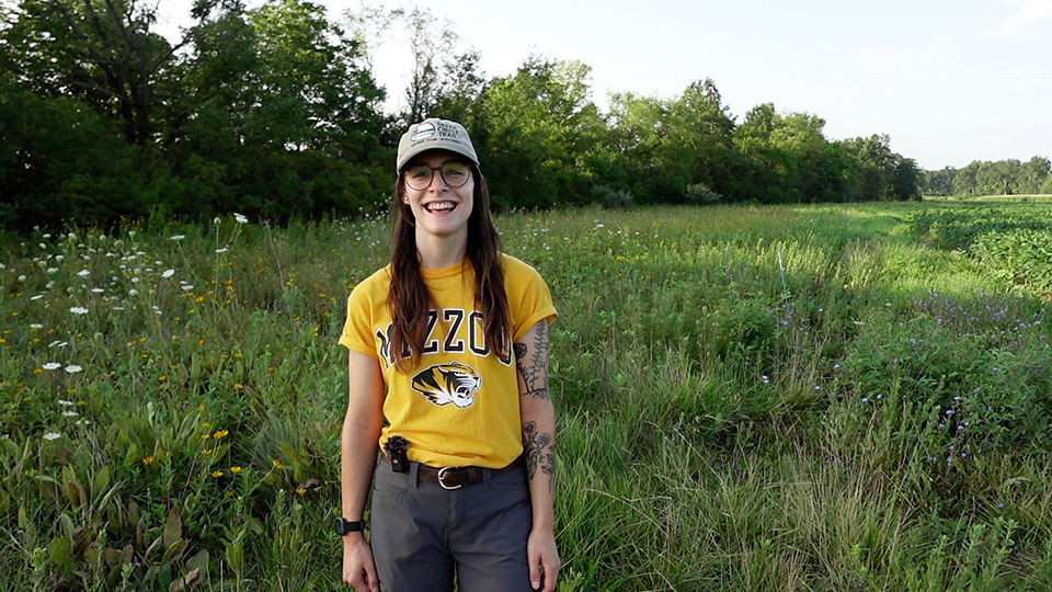 Leah Gastonguay poses in a field wearing a gold Mizzou shirt and a tan hat.