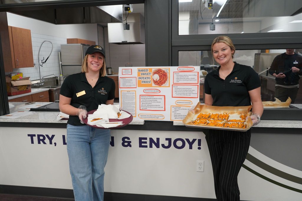 Two students pose with trays of food samples. 