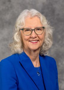 Portrait of Kendra Kattelmann in blue suit and glasses.