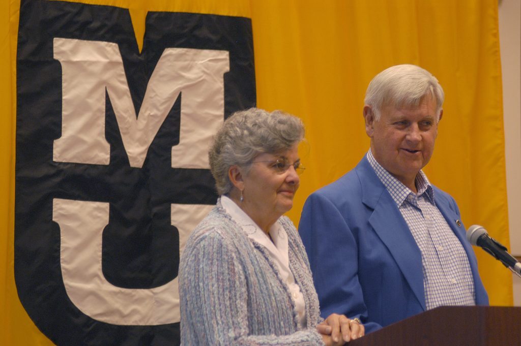 Mary Agnes and Al McQuinn at a podium with MU banner behind them.