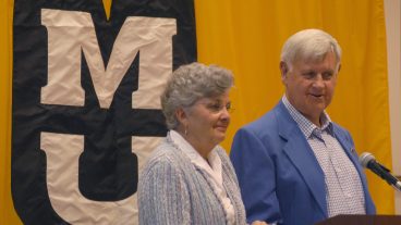 Mary Agnes and Al McQuinn at a podium with MU banner behind them.