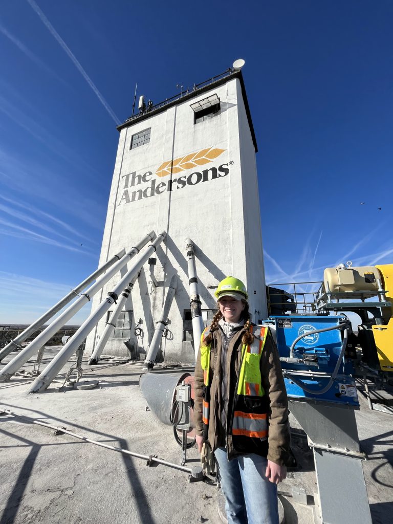 A woman poses for a photo in front of a grain bin. 