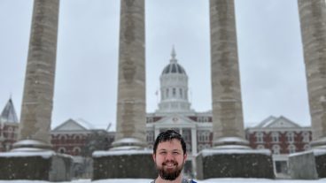 A student poses for a photo in the snow in front of the Columns.