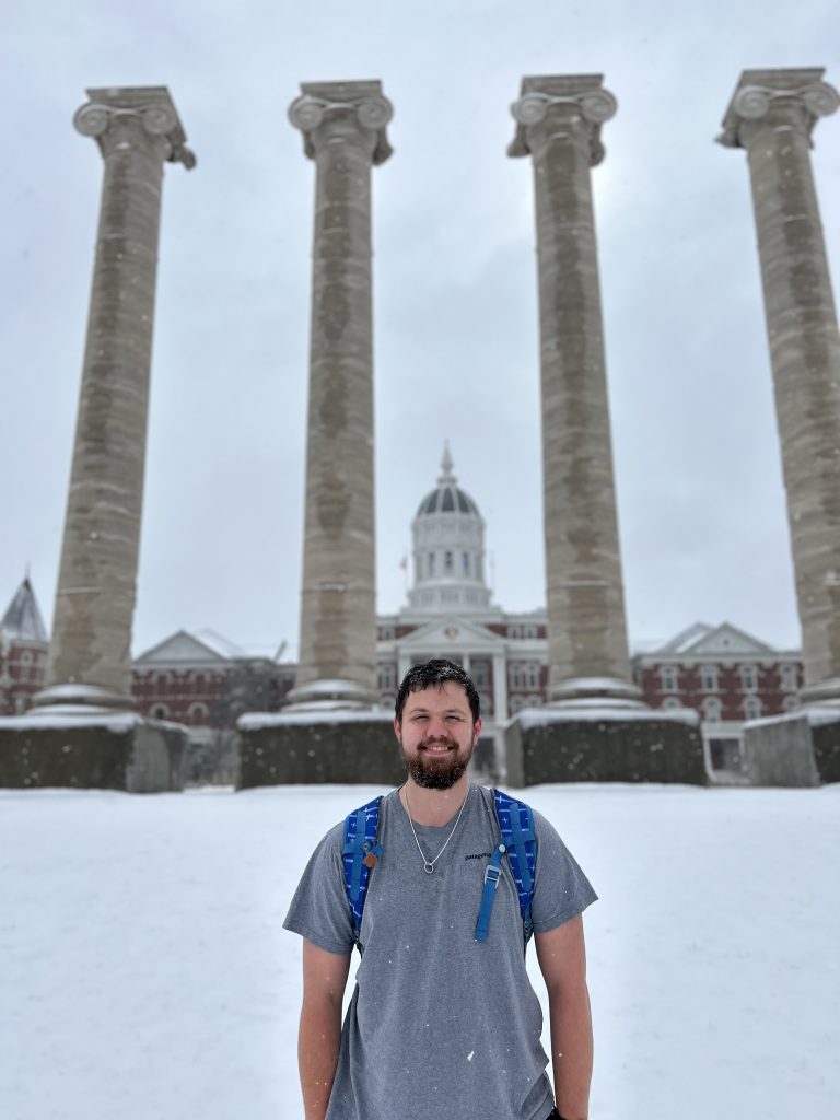 A student poses for a photo in the snow in front of the Columns. 