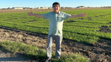 Jafar Tanin stands with arms outstretched in front of a field planted with wheat.