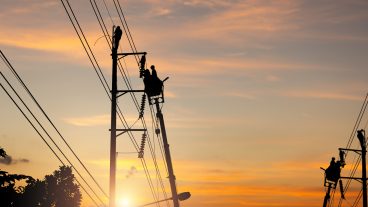 Silhouette of Electrical worker climbs a pole and uses a cable car to maintain a high voltage line system, Shadow of Electrician lineman repairman worker at climbing work on electric post