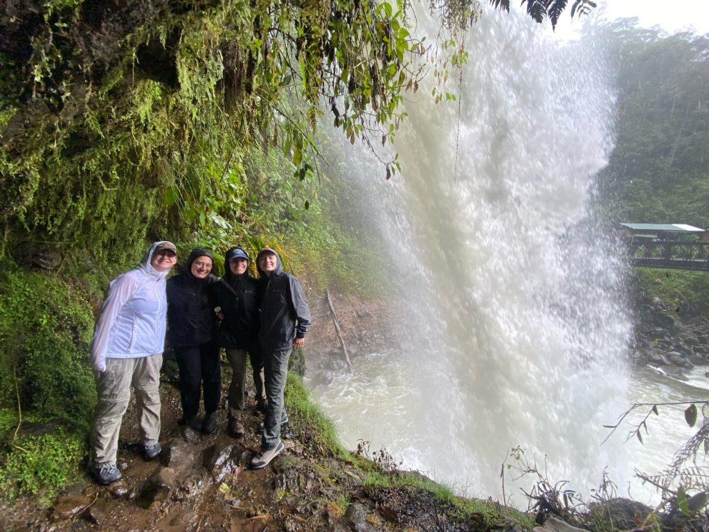 Four students stand near a waterfall. 