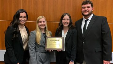 Four students pose with a plaque.