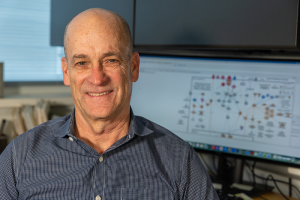Wes Warren sits in his office in front of a computer with charts displayed.