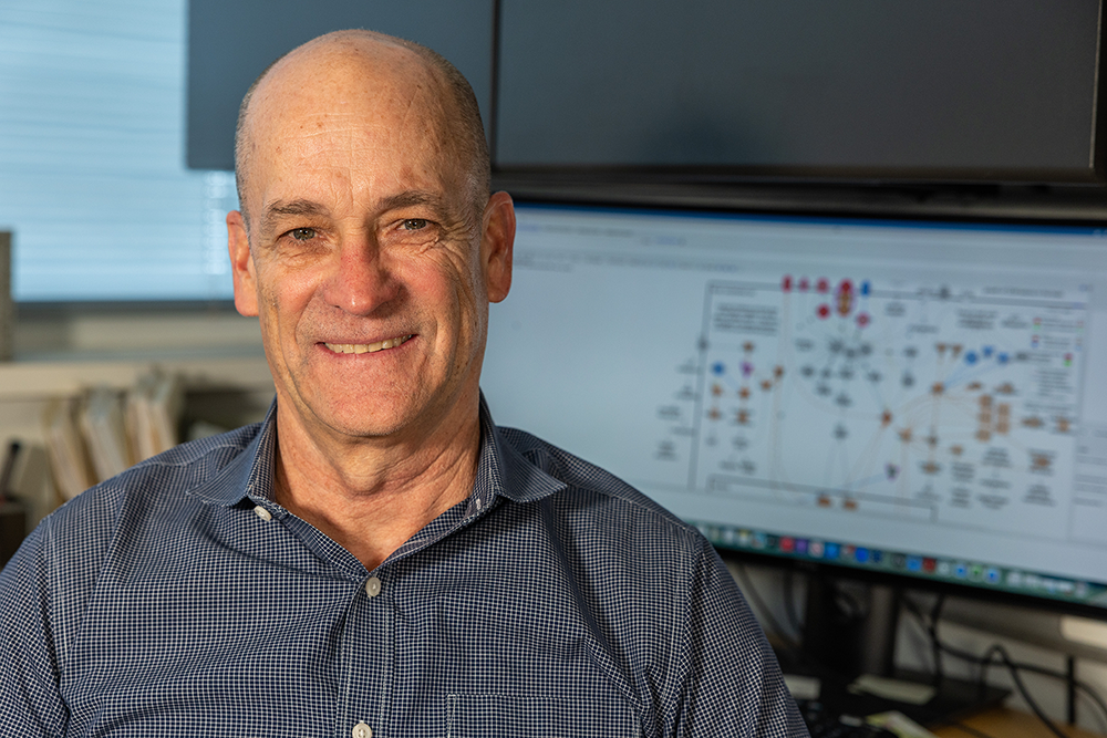 Wes Warren sits in his office in front of a computer with charts displayed.