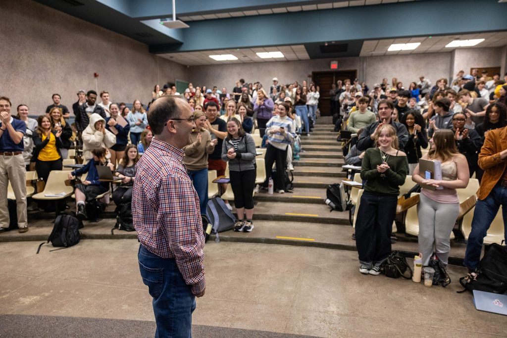 Eric Aldrich stands in front of his large class in an auditorium as they give him a standing ovation.