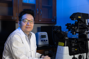 Kiho Lee is bathed in blue light as he sits in front of instrumentation in his laboratory.
