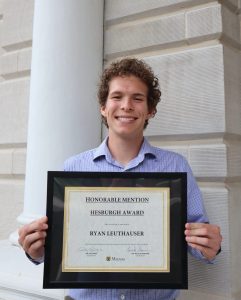 Ryan Leuthauser smiles and holds his Hesburgh Award.
