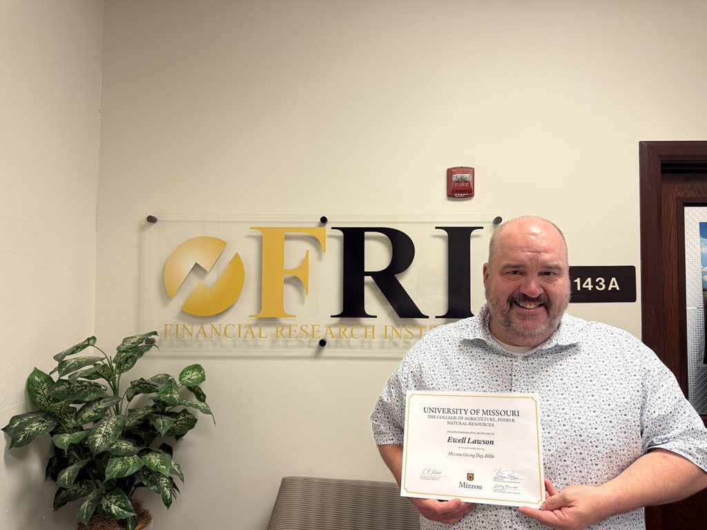 Ewell Lawson stands in front of the FRI (Financial Research Institute) sign holding a certificate for his gift on Mizzou Giving Day.