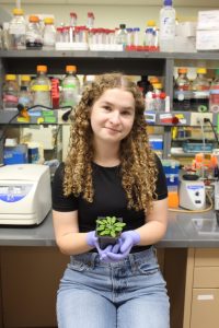 Carissa Bersche sits in a research lab and holds a small plant.