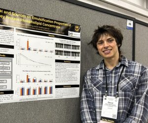 Oscar Bomgaars smiles and stands next to research poster.