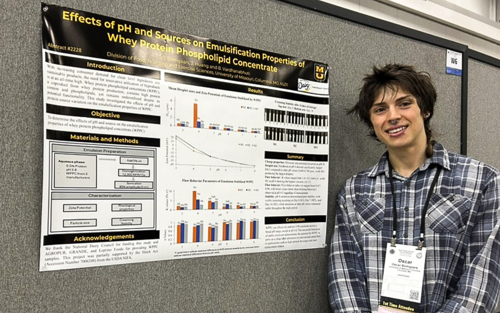 Oscar Bomgaars smiles and stands next to research poster.