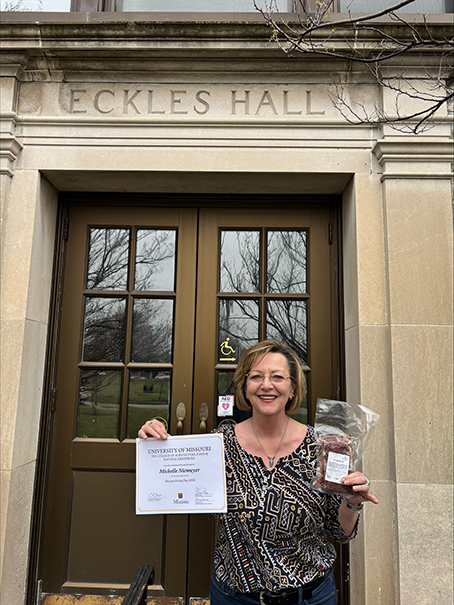 Michelle Niemeyer stands outside of Eckles Hall holding a certificate for her gift on Mizzou Giving Day.