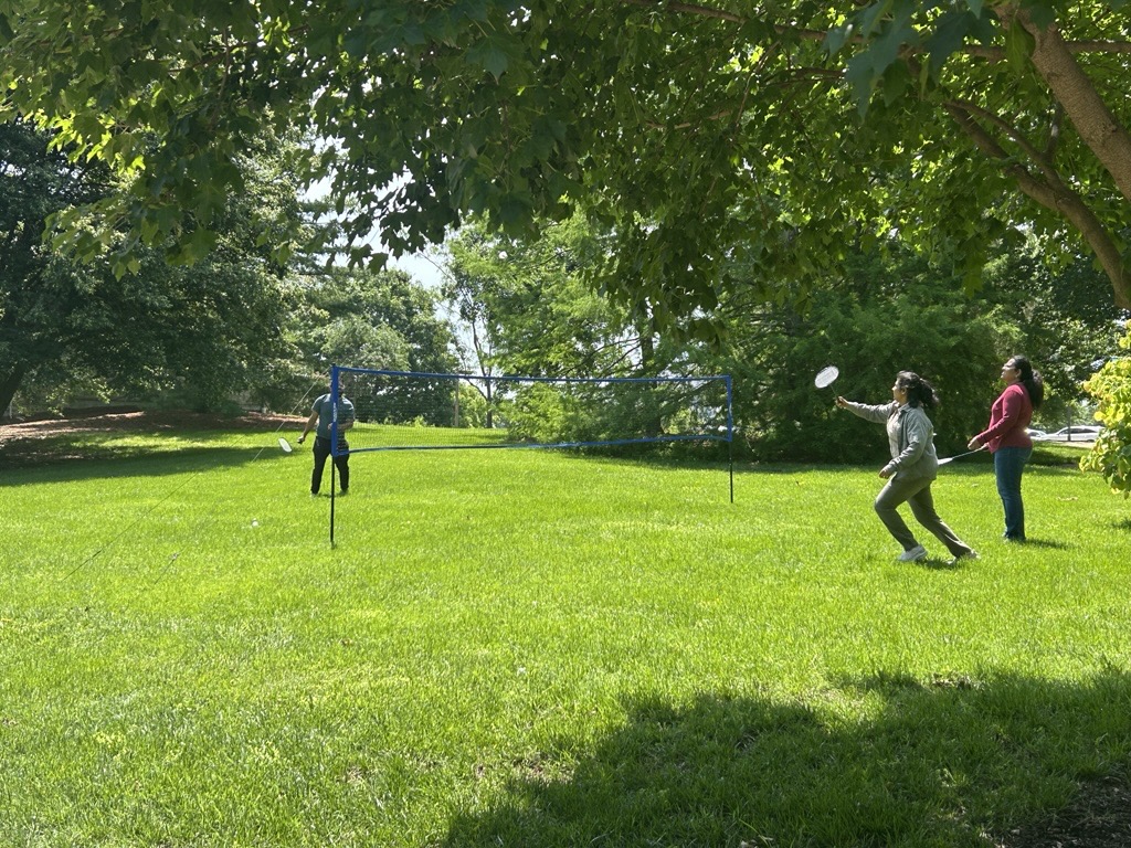 Participants play badminton on the sunny lawn.