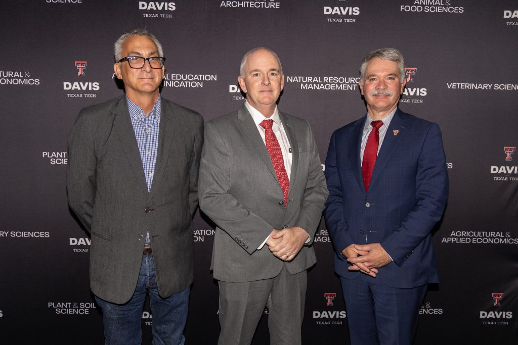 Three men, including Rick Relyea in the middle, stand in front of a banner with logos for the Davis College at Texas Tech University.
