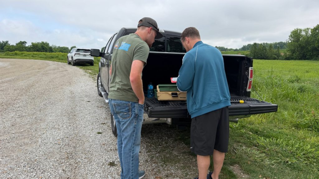 Reid Monsees looking at item with man on truck tailgate.