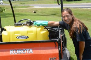 Chloe Stenger smiles next to a tank of fertilizer.