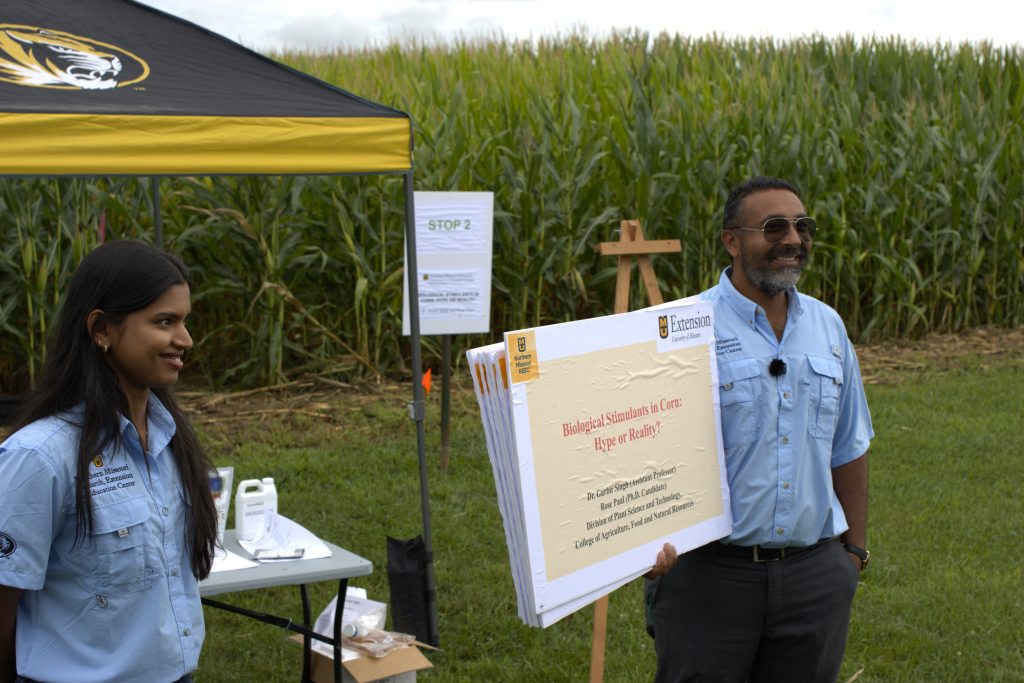 A man and young woman stand on either side of a poster.